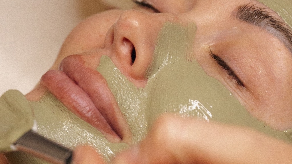 woman having a green face mask applied to face with a brush